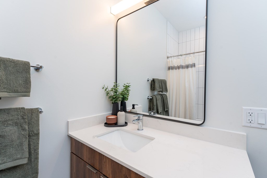 Modern bathroom at The Devon at Weiss Farm apartments in Stoneham, MA featuring quartz vanity, large mirror and tile tub.
