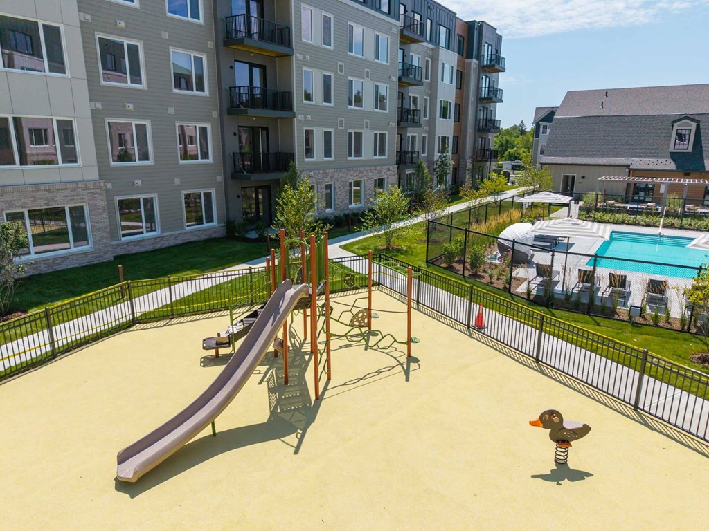Fenced playground with slide next to pool area at The Devon at Weiss Farm apartments in Stoneham, MA.