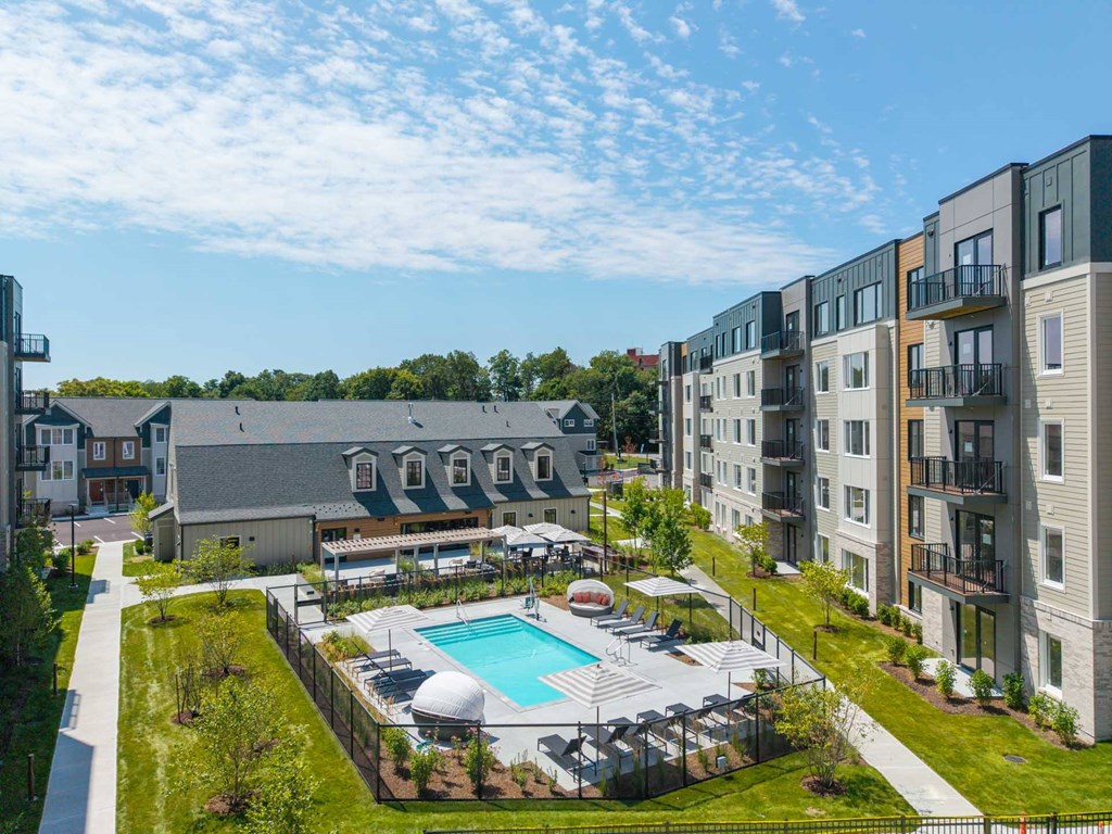 Aerial view of pool and amenity courtyard surrounded by apartments at The Devon at Weiss Farm in Stoneham, MA.
