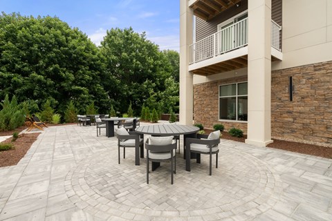 A patio with a table and chairs is surrounded by a stone wall and trees.