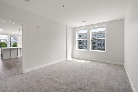 A spacious, empty room with a carpeted floor and two windows.
