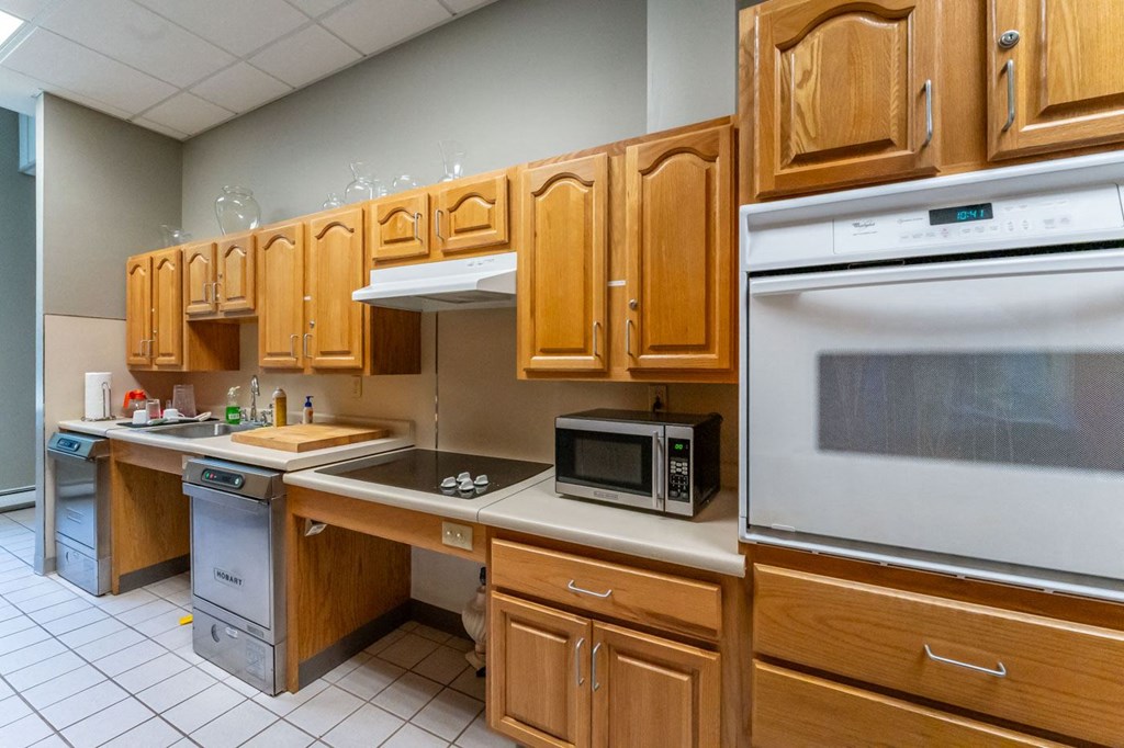a kitchen with wooden cabinets and a stove and a microwave in the community room