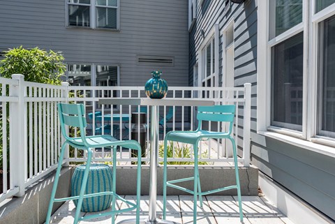 a small patio with blue chairs and a small table with a teal vase on it