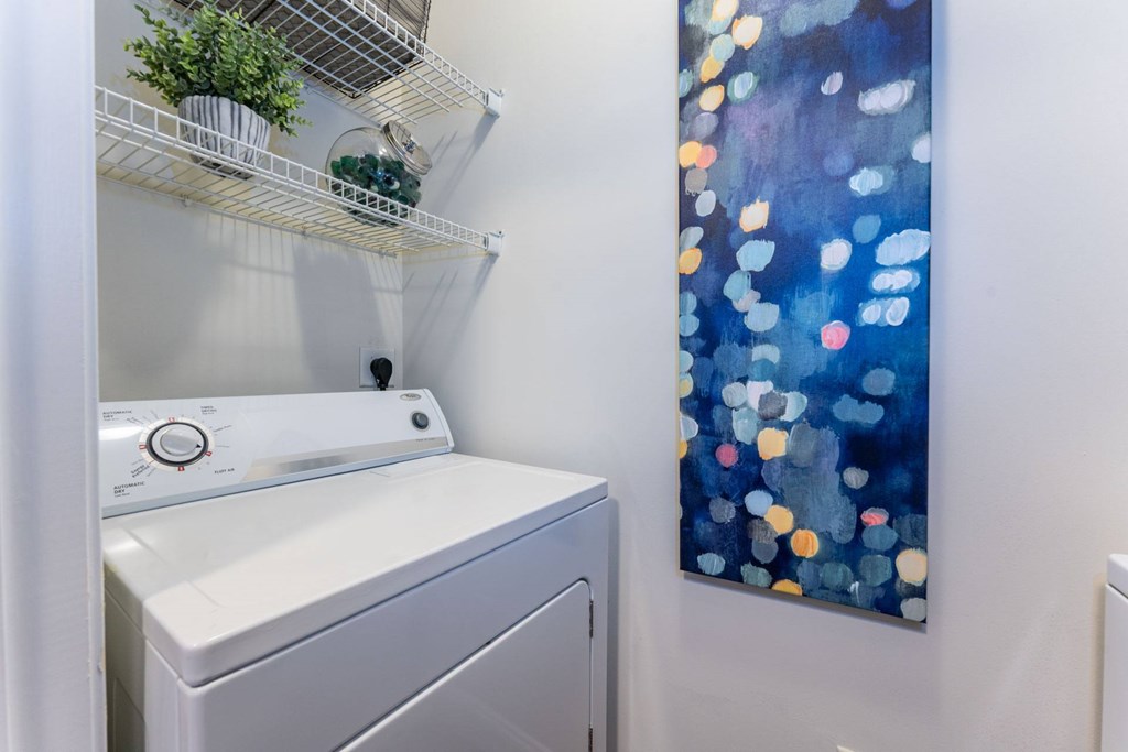 A washing machine is sitting next to a wall with a painting of blue and orange circles.