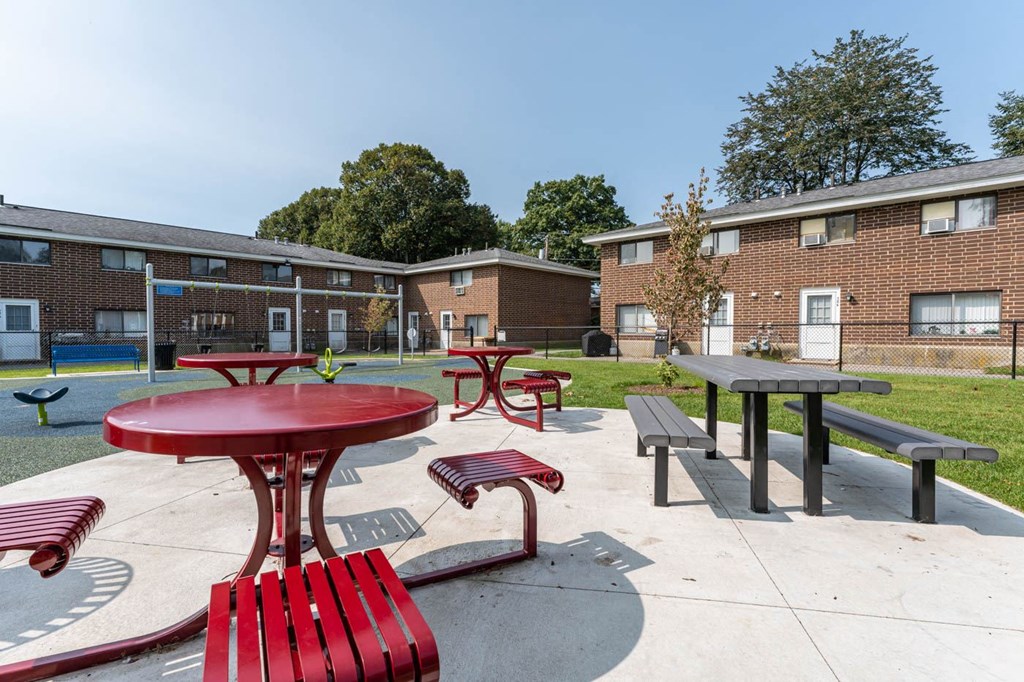 an outdoor picnic area with benches and tables in front of an apartment building
