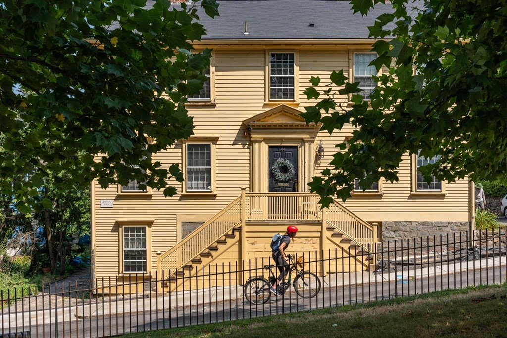 A person riding a bicycle in front of a yellow house.