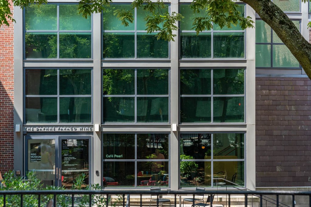 The exterior of a building with a glass facade and a tree in front.