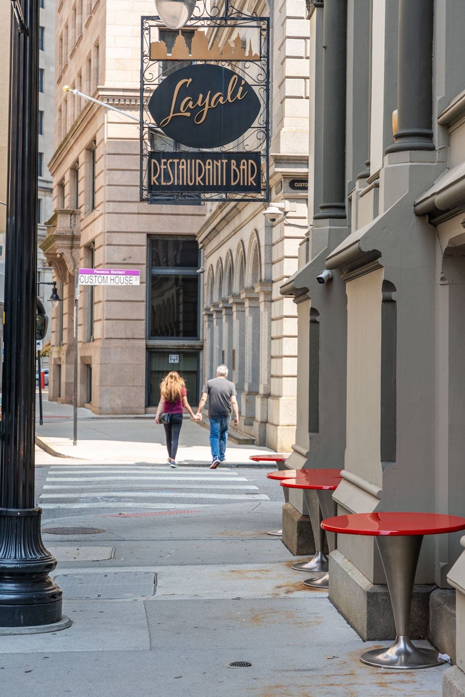 A couple walking down a sidewalk past a restaurant.