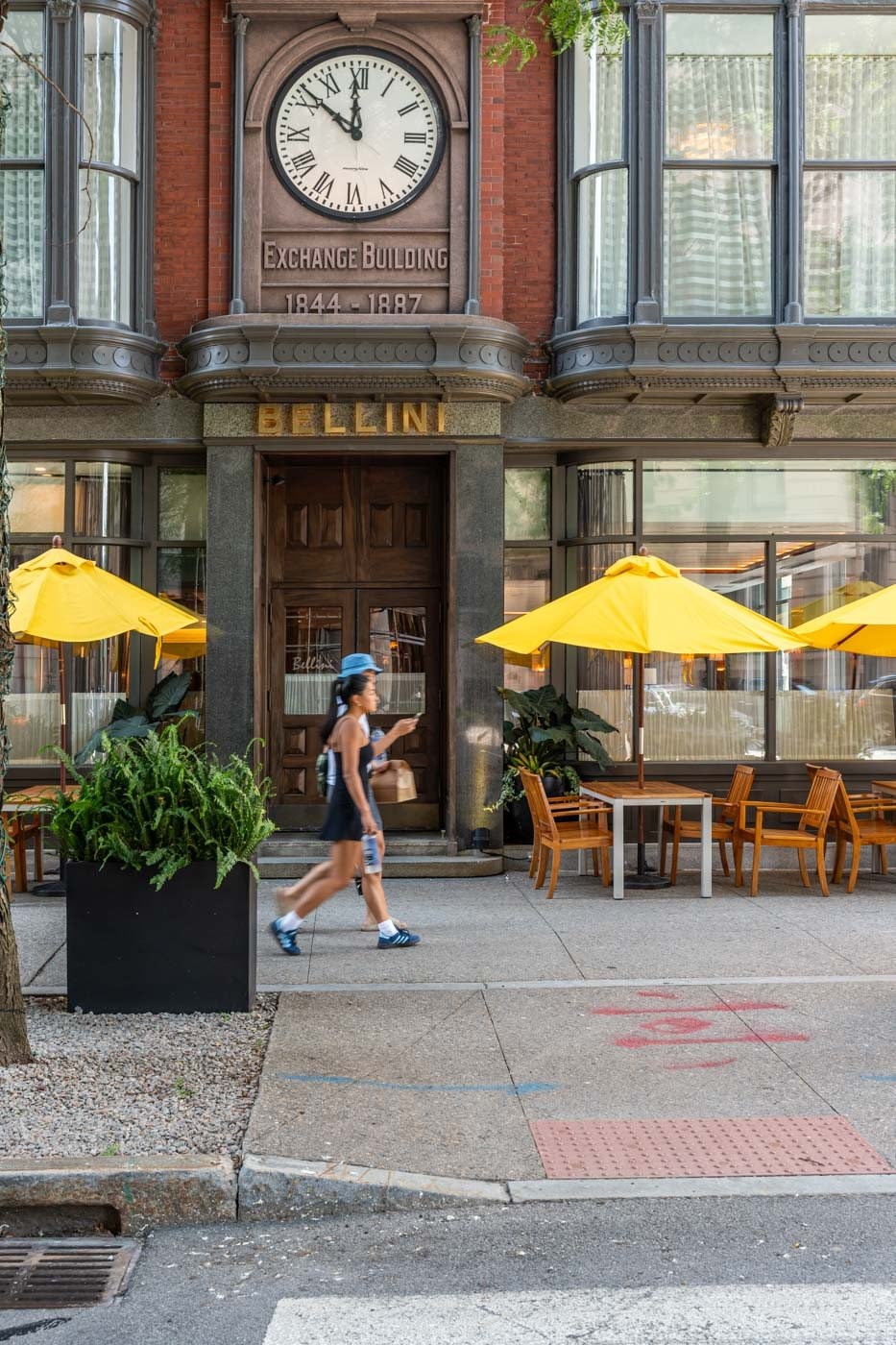 A woman is walking on the street in front of the Bellini Restaurant