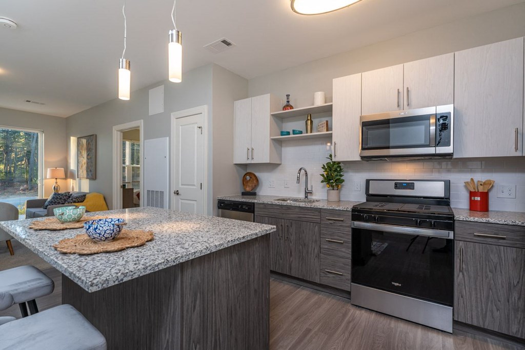 Redbrook model apartment with granite counters, stainless appliances, under cabinet lighting and kitchen island with hanging lights