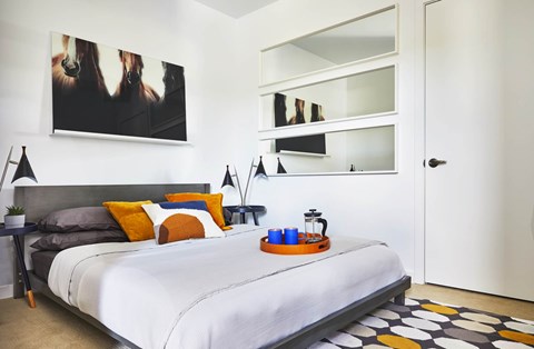 A bedroom with a bed, a nightstand with a tray on it, and a painting on the wall.