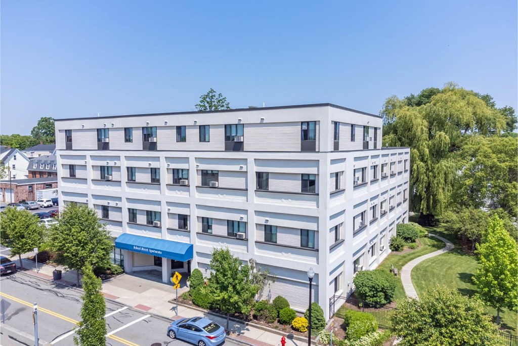 A modern building with a blue awning is surrounded by greenery and a clear blue sky.
