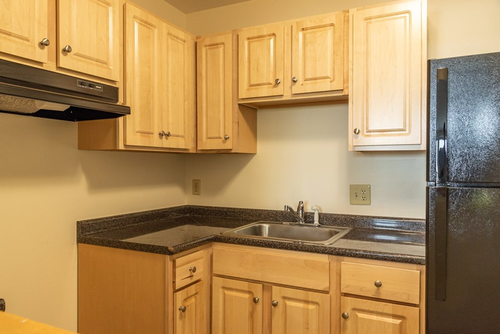 A kitchen with wooden cabinets and a black refrigerator.