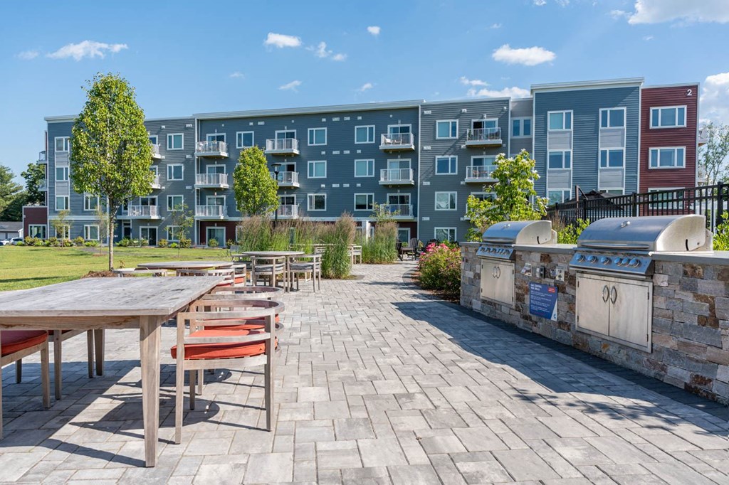 an outdoor patio with picnic tables and a barbecue grill at an apartment complex