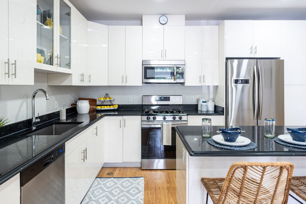 The sto one bedroom kitchen with black granite countertop, gas stove, stainless appliances, and white vibrant cabinetry