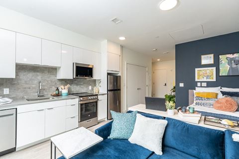a living room with a blue couch and a kitchen with white cabinets and stainless steel appliances at Union 346 Apartments, Somerville, Massachusetts