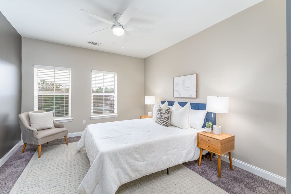 A bedroom with a bed, chair, and ceiling fan.