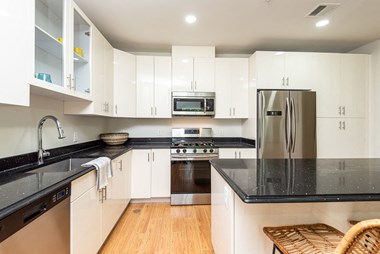 The sto one bedroom kitchen with black granite countertop, gas stove, stainless appliances, and white vibrant cabinetry
