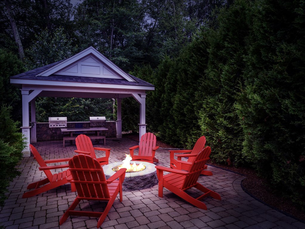A gazebo with red chairs and a fire pit in the middle of a patio.