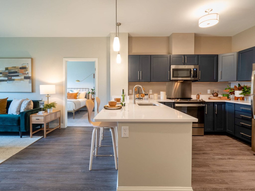 A sleek kitchen with quartz countertops, pendant lighting, and dark cabinetry equipped with stainless steel appliances.