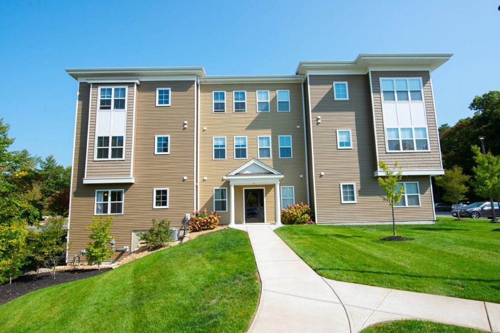 The main entrance to Webster Woods, featuring a sidewalk leading to a contemporary apartment building with clean, modern lines.