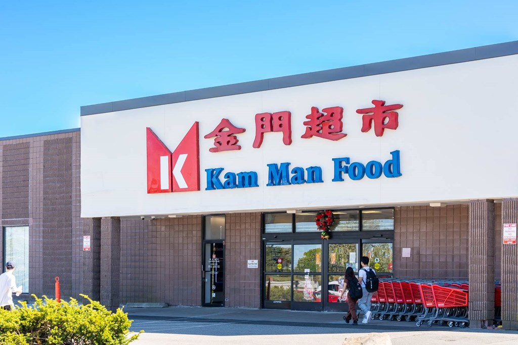 A storefront of a Kam Man Food store with people walking by.