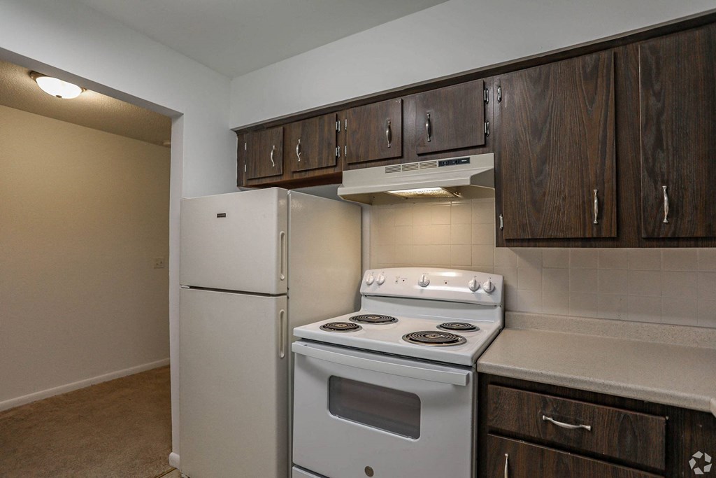A kitchen with brown cabinets and white appliances, including a white refrigerator, dishwasher, electric range, and garbage disposal.