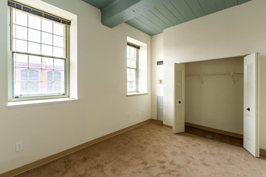 A room with a carpeted floor, a window, and a closet.