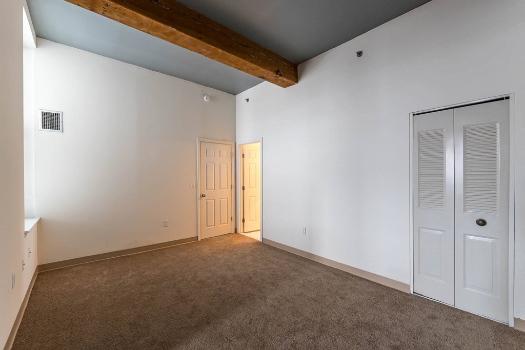 A room with a brown carpet and a wooden beam on the ceiling.