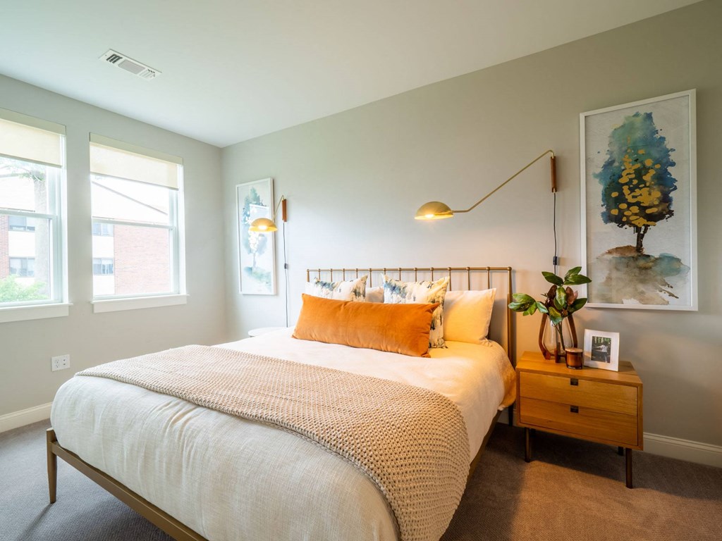 A cozy and well-lit living space that opens to a bedroom with soft furnishings and chic lighting.