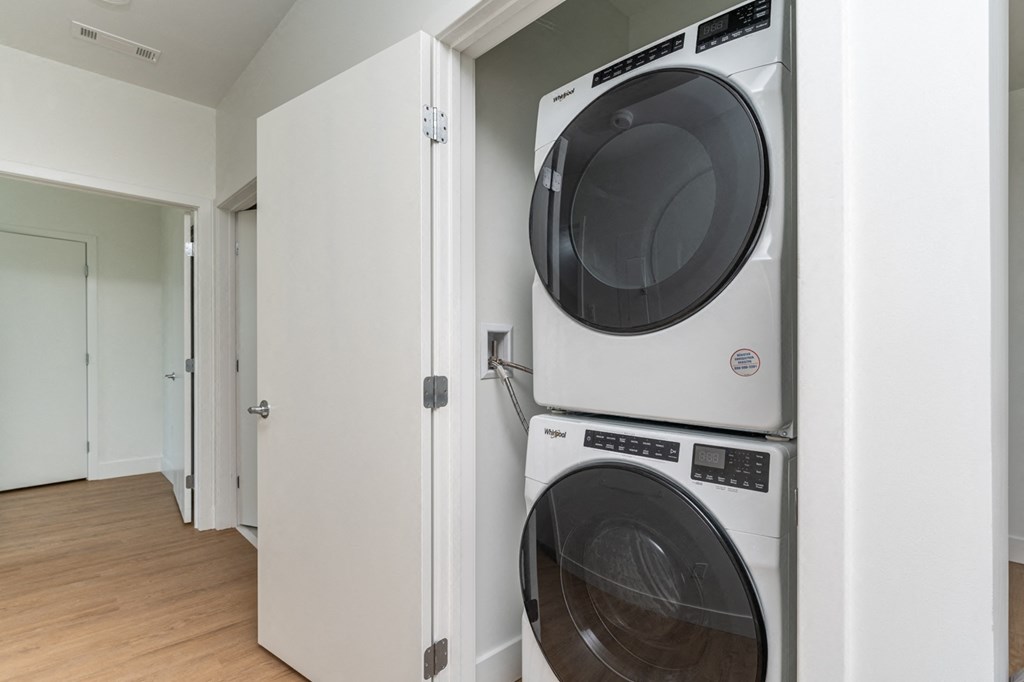 A white dryer and washer are stacked on top of each other in a small laundry room.