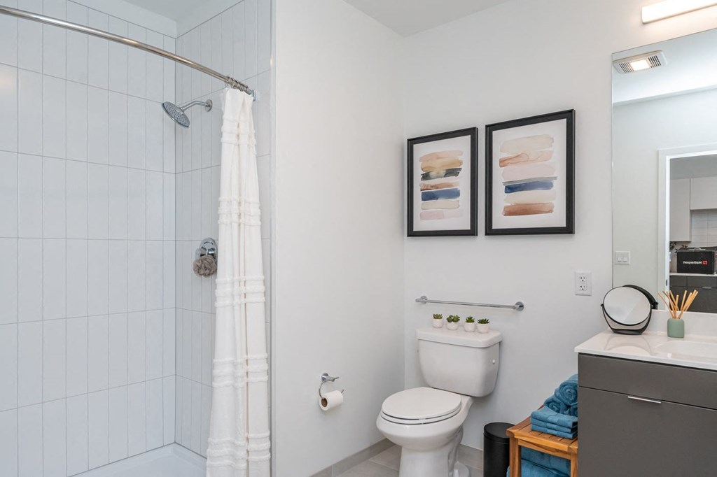 A white toilet sits next to a white shower curtain in a small bathroom.