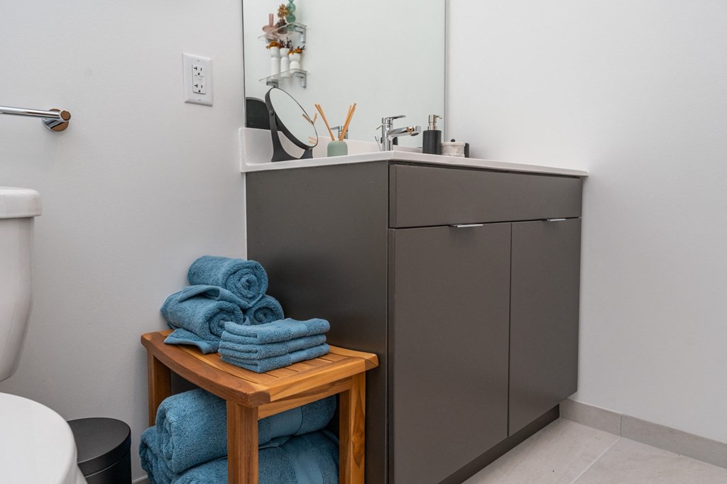 A bathroom with a grey cabinet, a white sink, and a wooden table with blue towels on it.