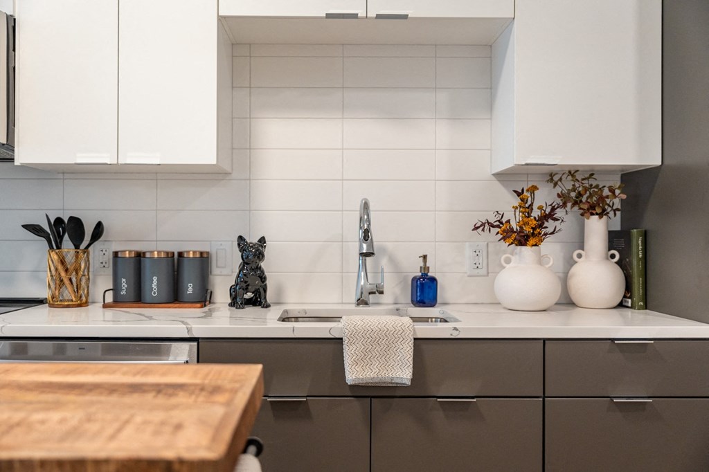 A kitchen with white cabinets and a wooden cutting board on the counter.