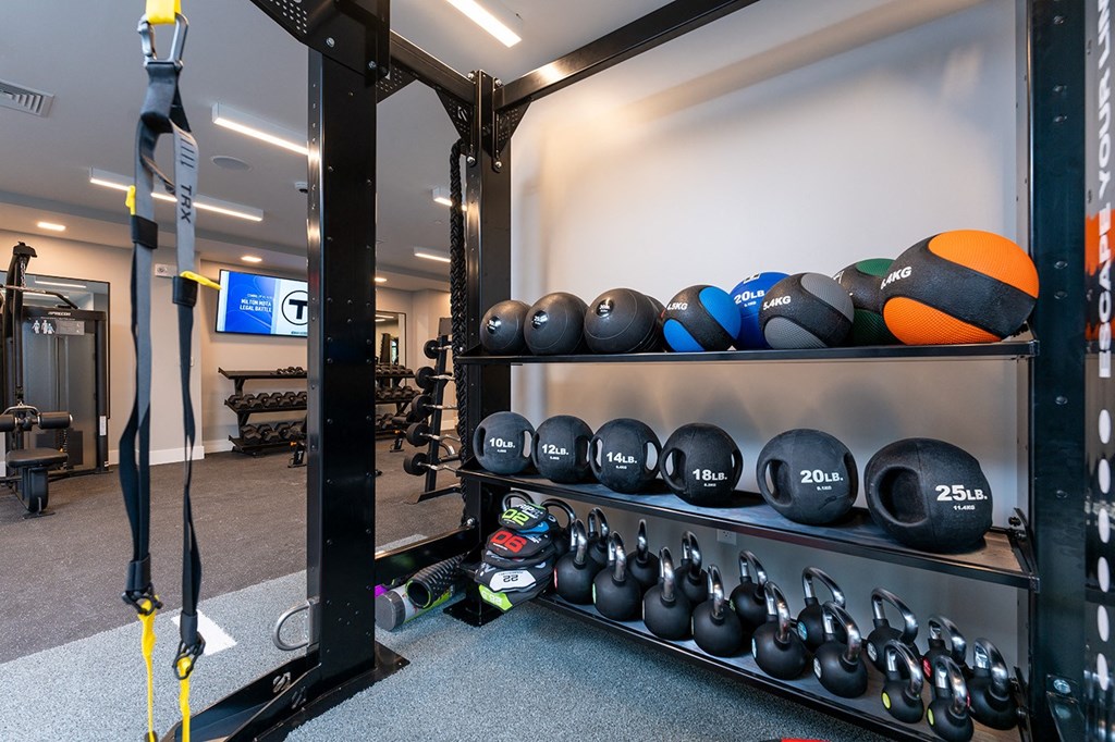 A gym with a rack of kettlebells and a yellow pull up bar.