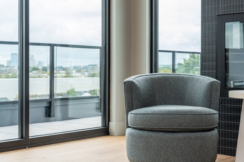 A grey chair is in front of a window with a view of a cityscape.