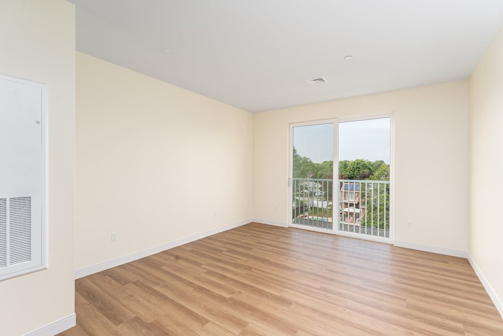 Unfurnished living area with wood-style plank flooring and tall sliding-glass doors that open to a balcony overlooking the neighborhood.