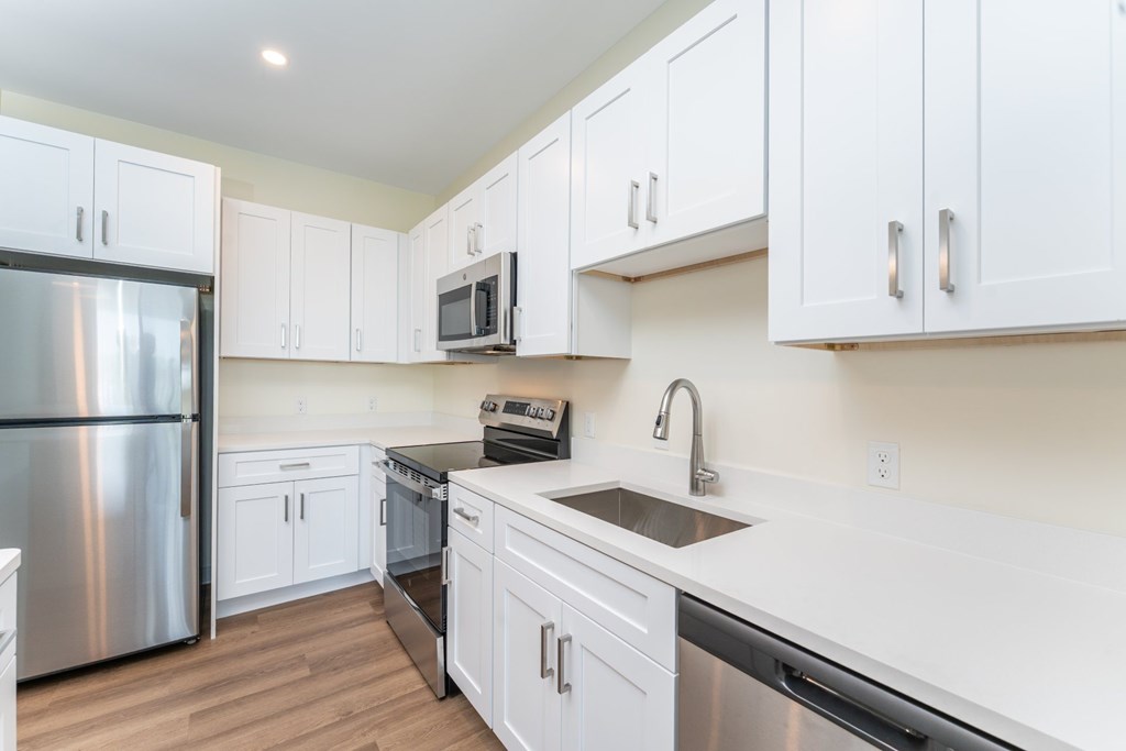 Close view of a white-quartz kitchen counter with undermount sink, gooseneck faucet and surrounding stainless appliances.