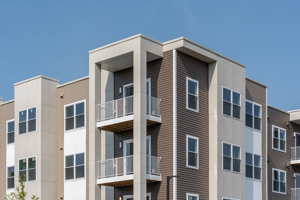 Detail of building façade showing stacked private balconies, taupe siding and vertical columns against a clear blue sky.