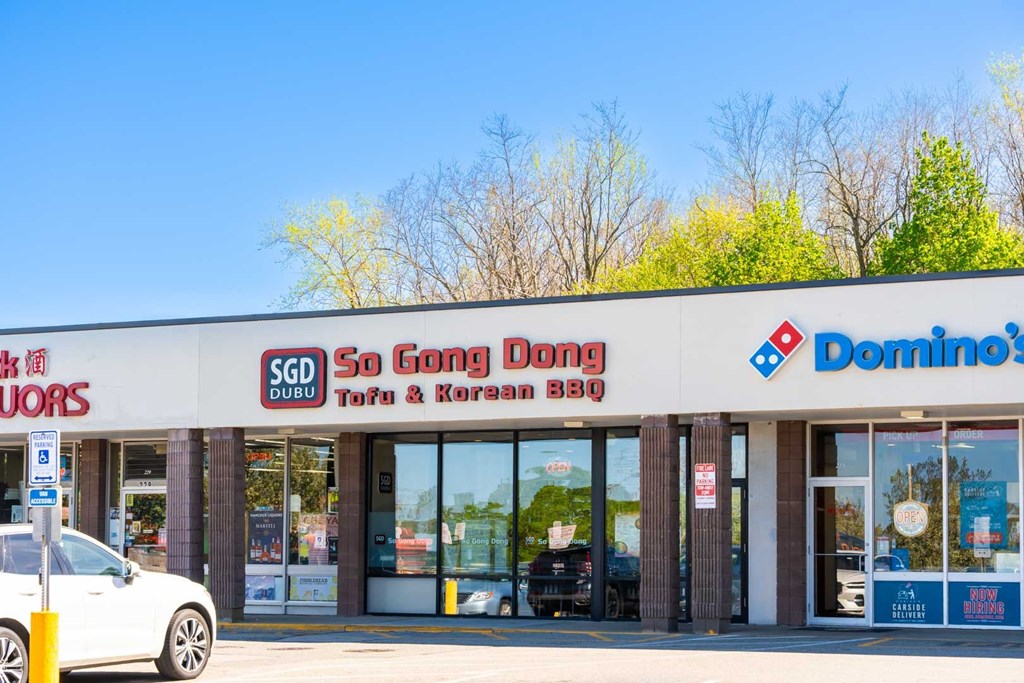 A white car is parked in front of a store with a sign that reads