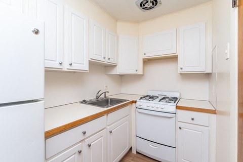 A white kitchen with a stove, sink, and cabinets.