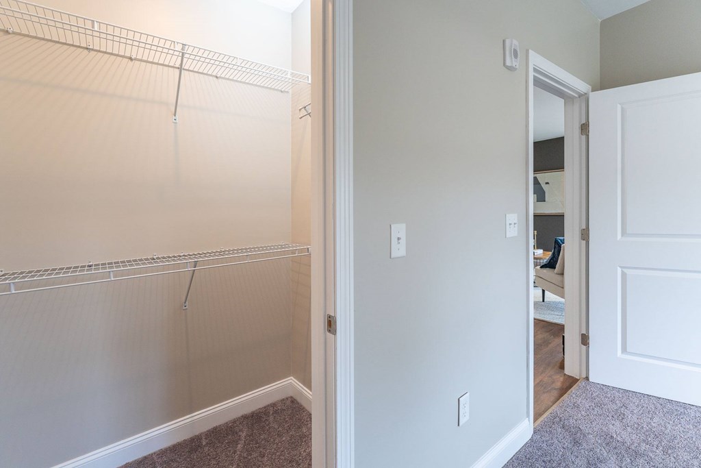 A white door is open to a hallway with a white wall and a grey carpet.