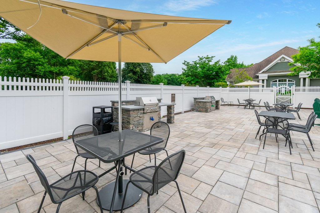 the patio has a grill and tables with chairs and umbrellas at Woodlands at Abington Station, Abington, MA, 02351