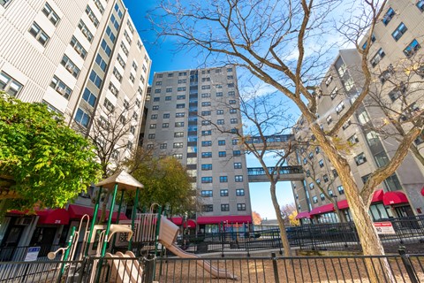 A playground with a slide and a tree in front of apartment buildings.