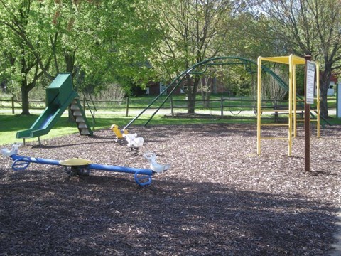 A playground with a green slide, a yellow swing set, and a blue seesaw.