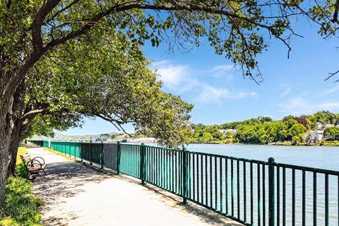 A green fence runs along a walkway next to river walk at water at Brewery Square Apartments, New Haven , CT