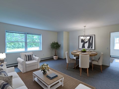 A living room with a white couch, a coffee table, a dining table with chairs, and a potted plant.