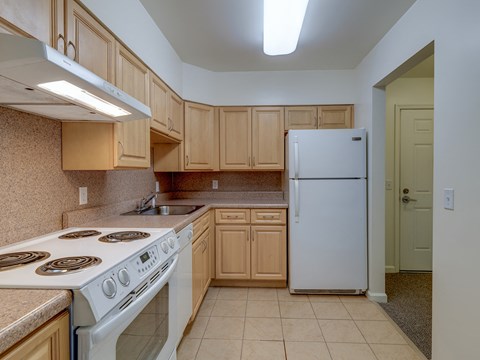 A kitchen with a white stove top oven, white refrigerator, and wooden cabinets.
