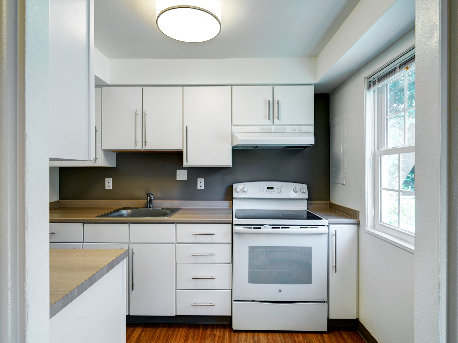 A white kitchen with a stove, sink, and cabinets.