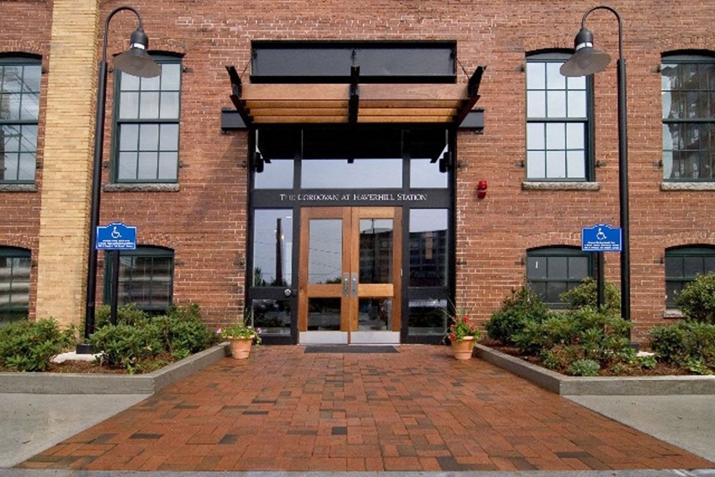 The entrance to a brick building with a wooden overhang and a sign that reads at The Cordovan at Haverhill Station, Haverhill, MA